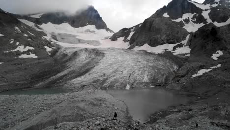 Aerial-flyover-over-a-hiker-towards-the-Witenwasseren-glacier-and-its-glacial-lake-in-Uri,-Switzerland