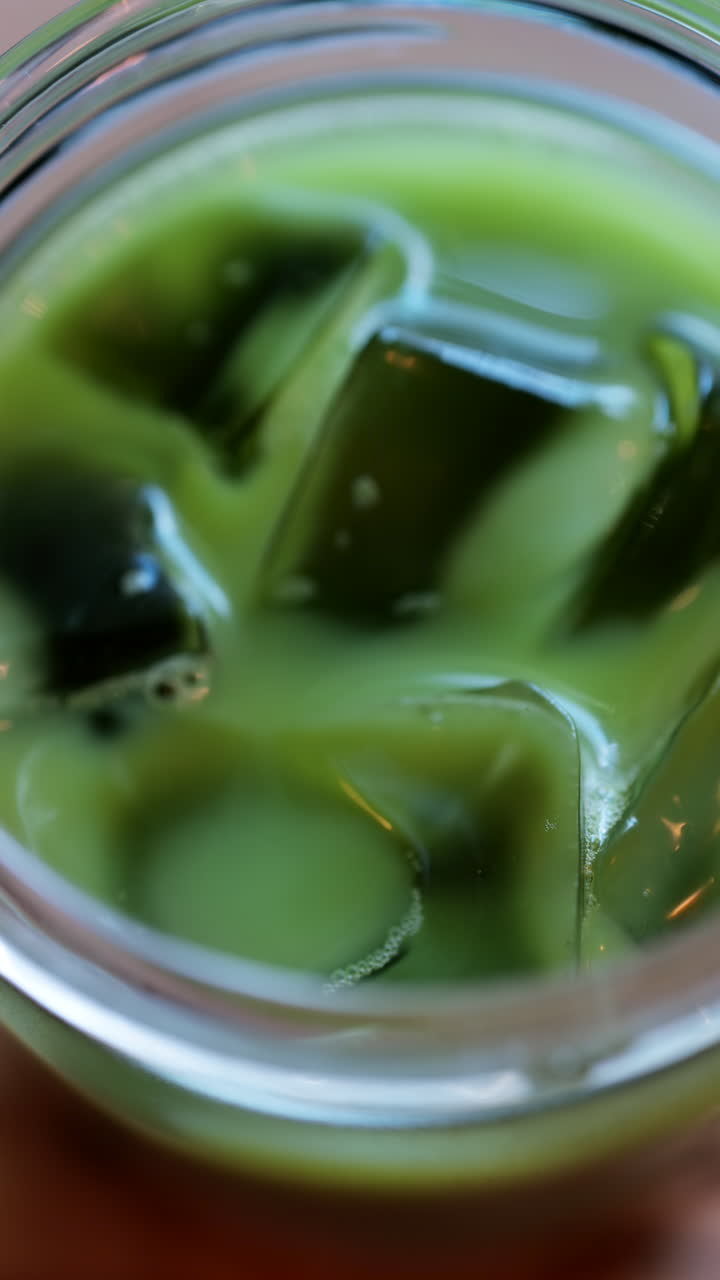 Close up of a glass of an iced matcha on a table at a cafe. Vertical