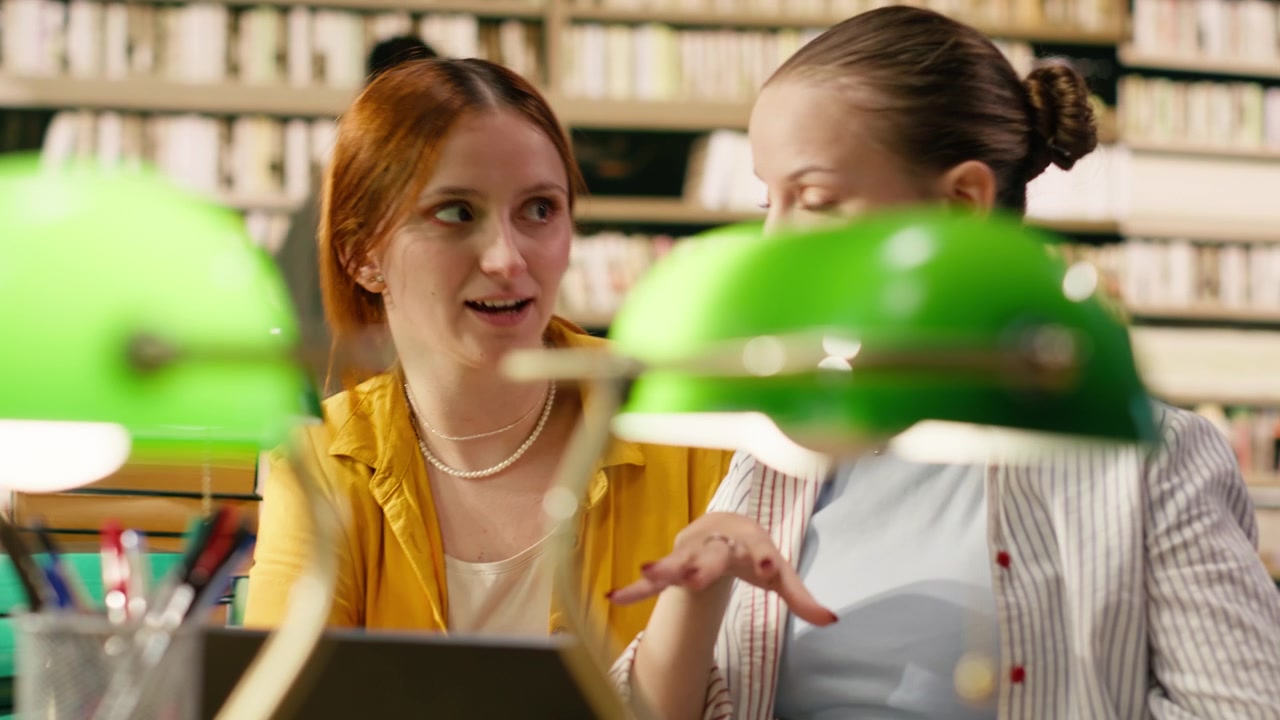 Mentor guiding student through academic work on laptop at library table