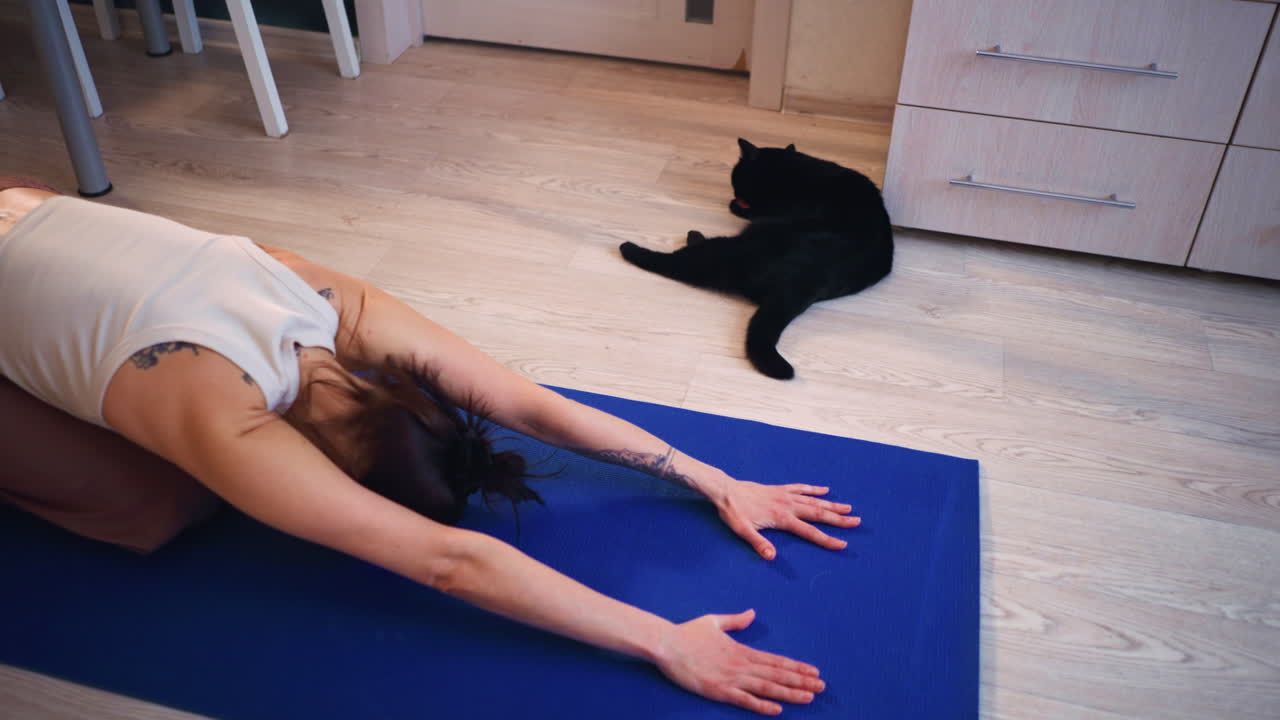 Caucasian Wellness Coach Practicing Yoga Near Black Cat On Blue Mat, ChildSPose Style Stretch With Candlelit Calm, Serene Home Studio Vibe, Mindful Breath And Companion Presence