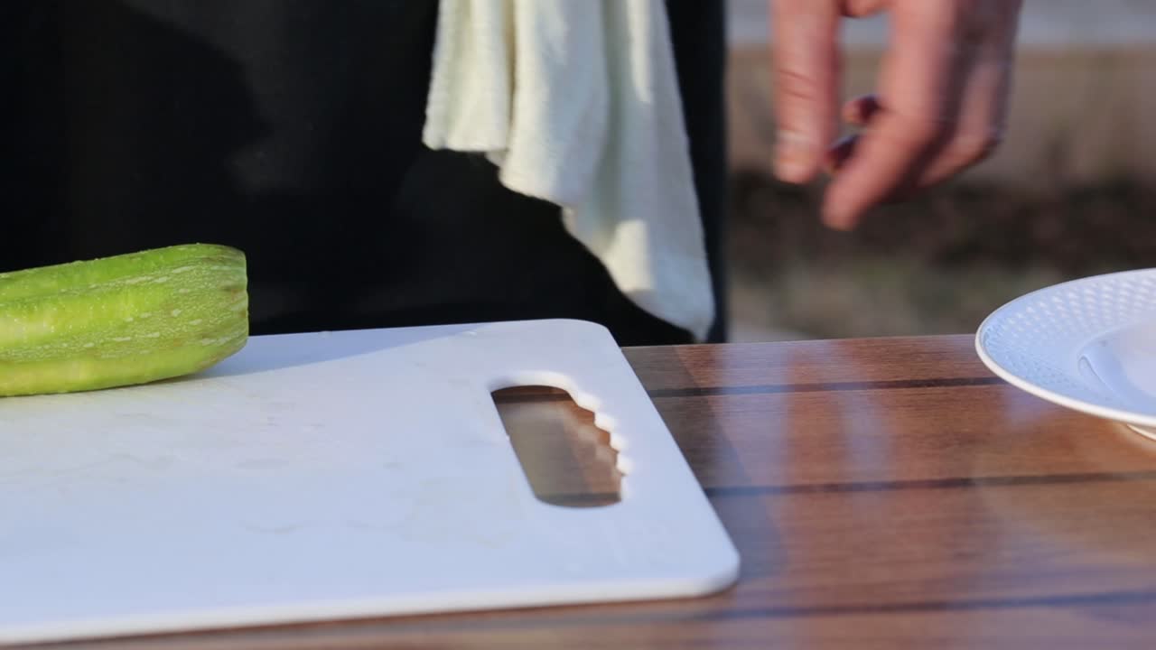 A person's hand holding a knife cuts a ribbed ketolla gourd or luffa acutangula or gambas on a wooden cutting board