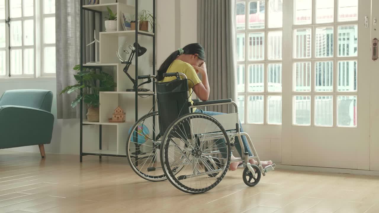 Disappointed Asian Kid Girl  Sitting In A Wheelchair Near Door In The House