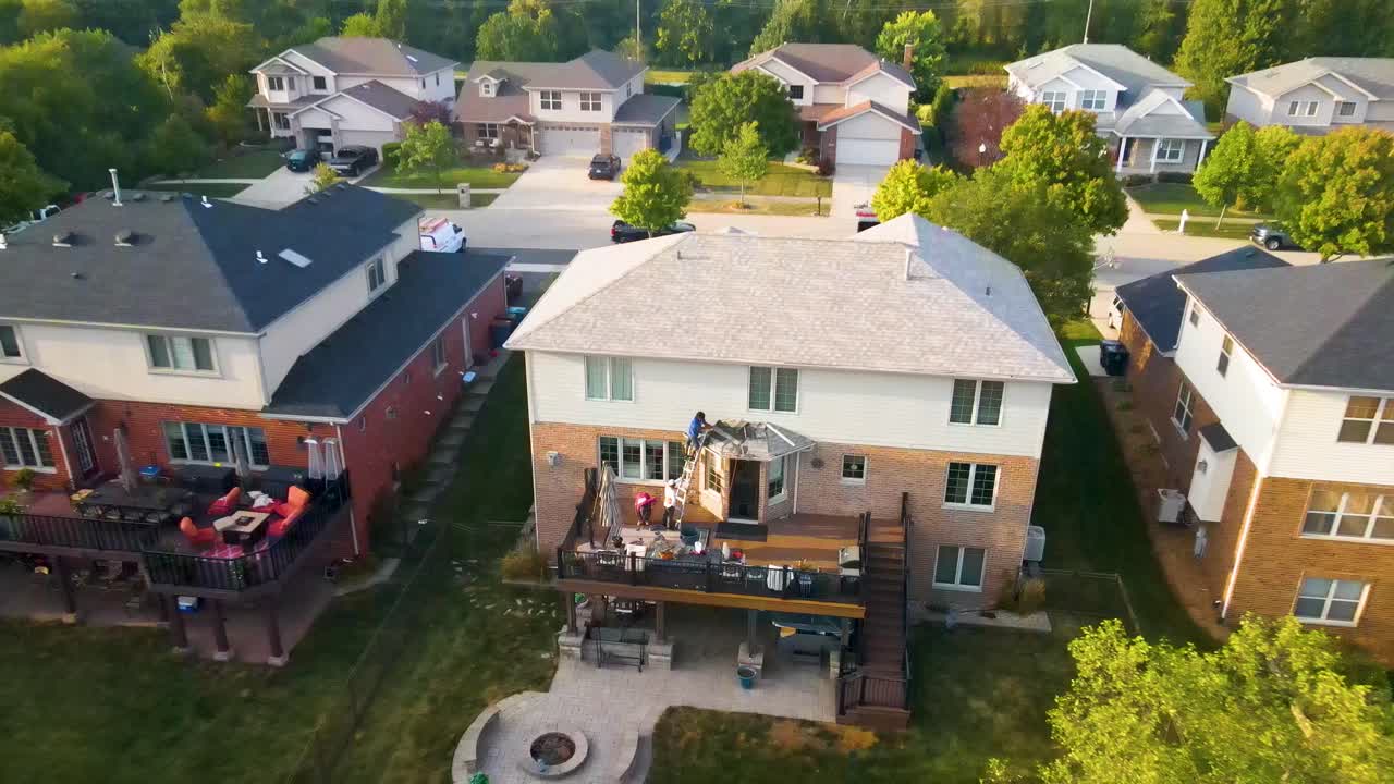 Aerial view of construction workers laboring in a backyard patio with outdoor furniture, a fire pit, and a well-maintained lawn, showcasing a cozy and inviting outdoor living space.