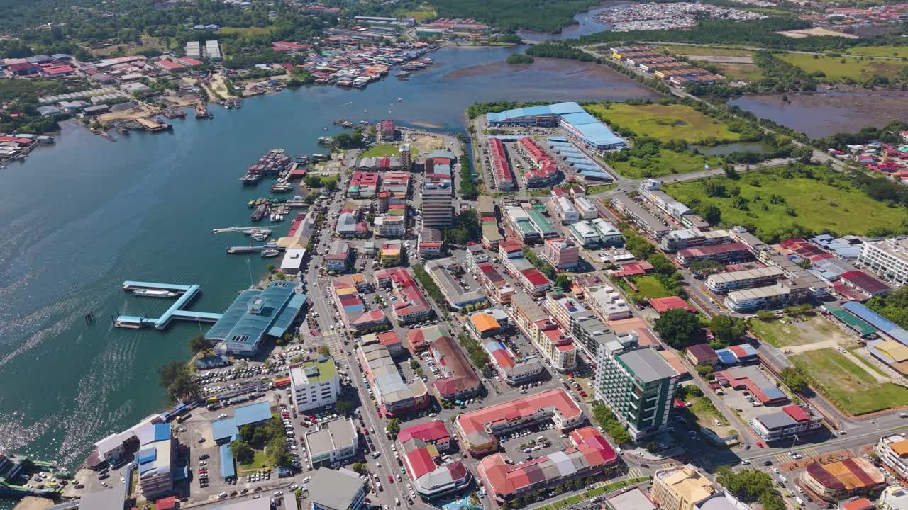 Slow drone shot of Victoria cityscape in Labuan, Malaysia, showcasing coastal urban life, waterways, and vibrant architecture under bright tropical sunlight