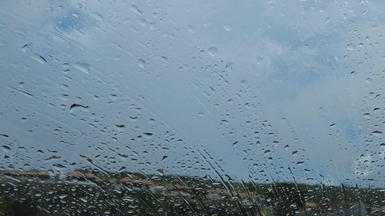 집과 구름이 배경에 있는 자동차 앞유리와 창문에 떨어지는 빗방울의 근접 촬영