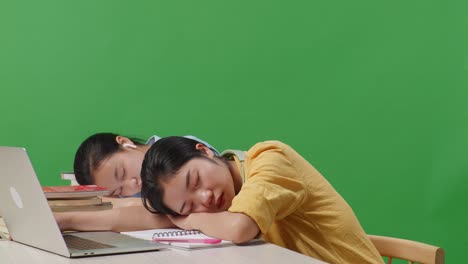 close up of asian woman students sleeping on a table with a laptop while studying in the green screen background classroom