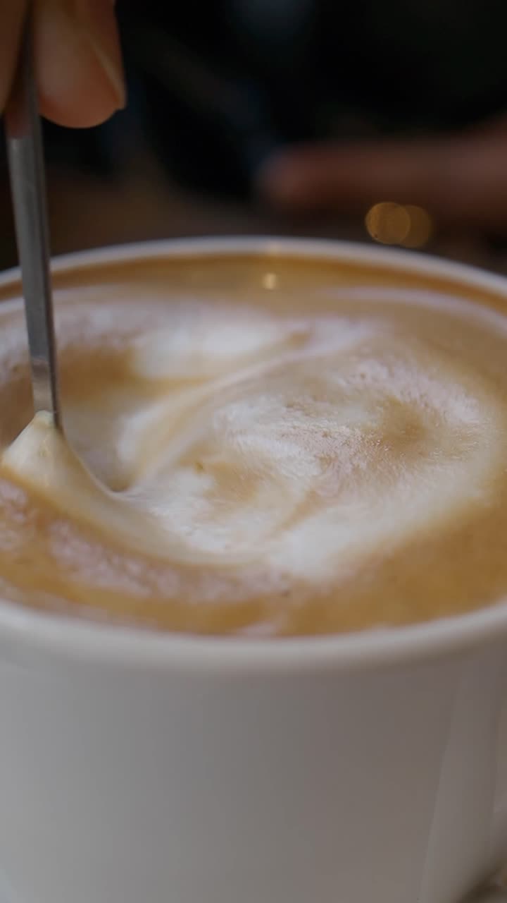 Primo piano di una mano che mescola caffè cremoso in una tazza bianca