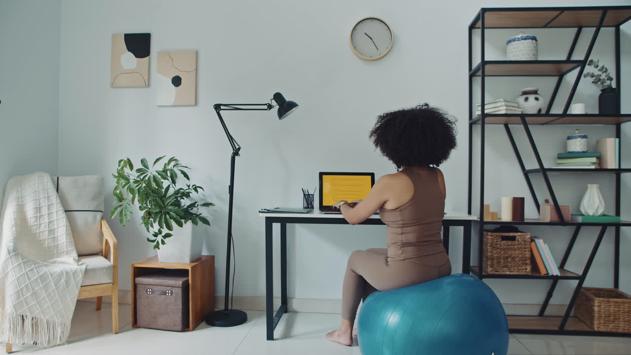 Female Freelance Worker Coding on Laptop on Fitness Ball at Home