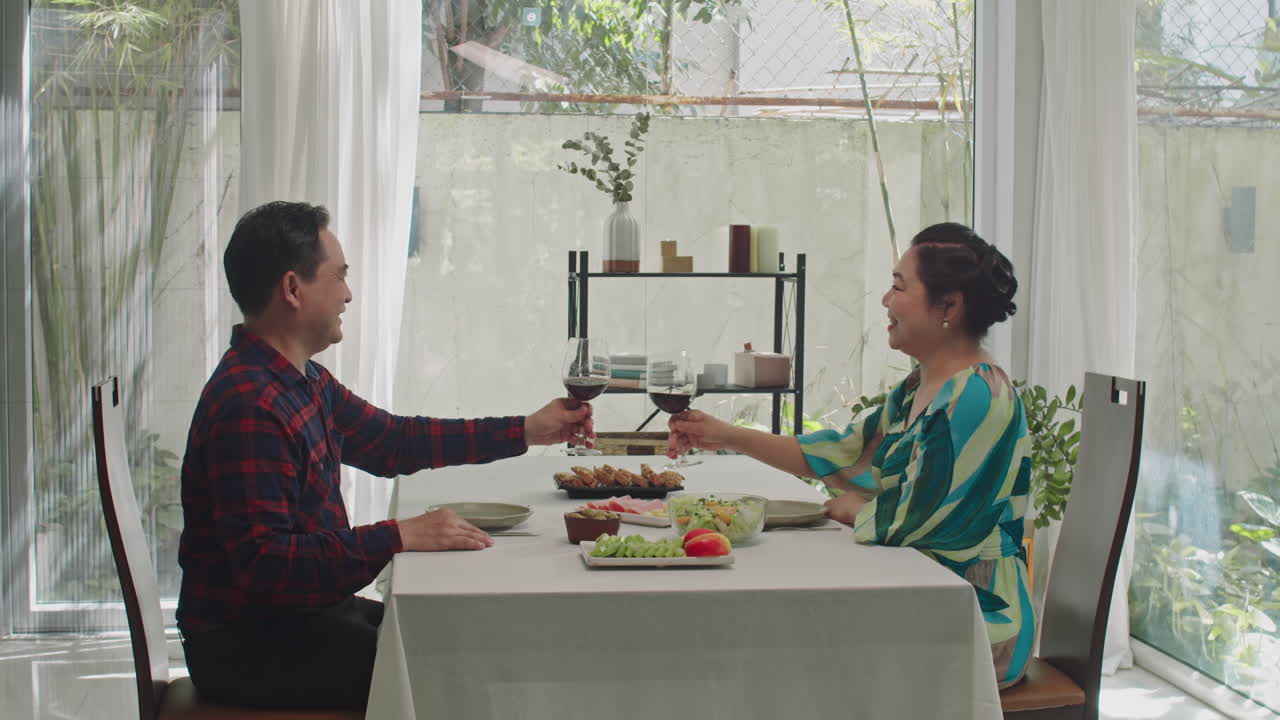 Retired Man and Woman Clinking Glasses during Romantic Dinner at Home
