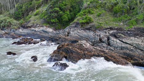 dynamic ocean waves crash against rugged rocks, surrounded by lush greenery, under natural daylight at charlesworth bay, australia
