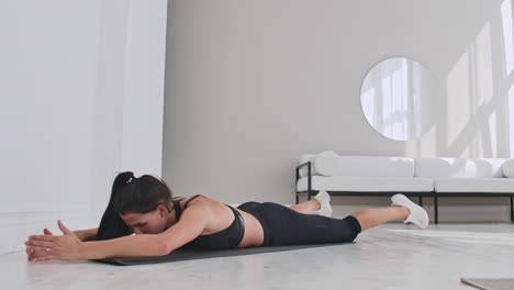 joven mujer atractiva en doble pierna patadas ejercicio estudio gris. joven mujer atractivo practicando yoga estiramiento en doble piernas patadas ejercicio