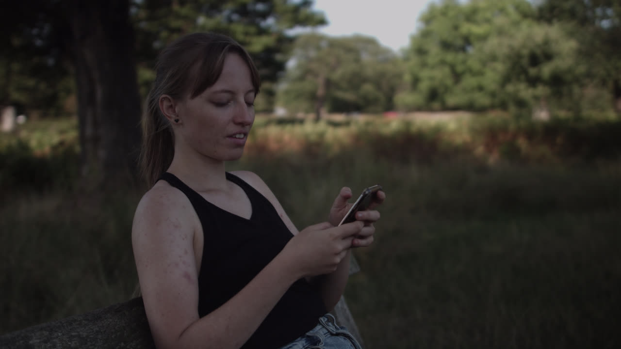 el primer plano de una mujer joven que toma varias fotografías del hermoso paisaje del parque mientras está de pie a la sombra de un árbol