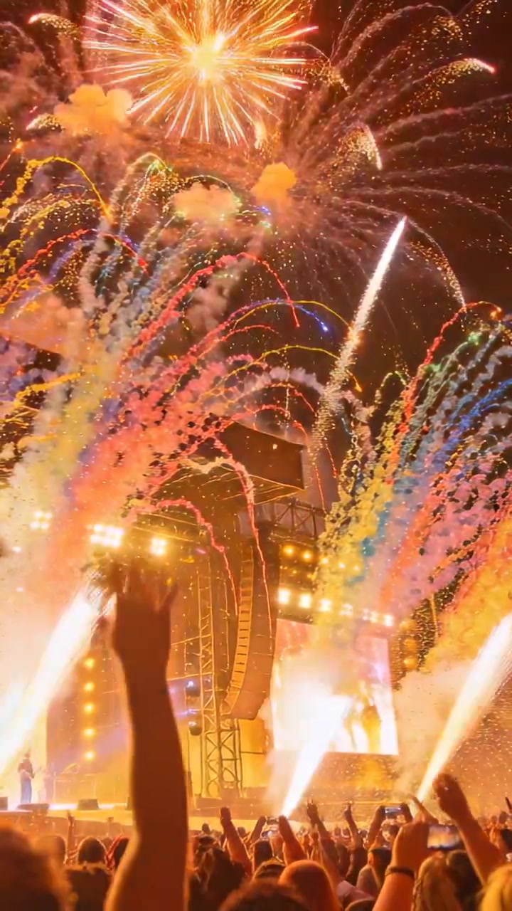 Pystyvideo: Ilotulitusraketteja laukaistaan, lava lähettää purskahduksia illan konsertin finaalissa, puhelimet kuvaavat.