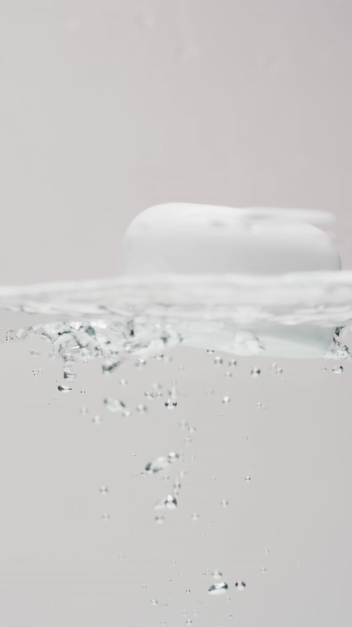 Vertical video of beauty product tub falling in water with copy space on white background