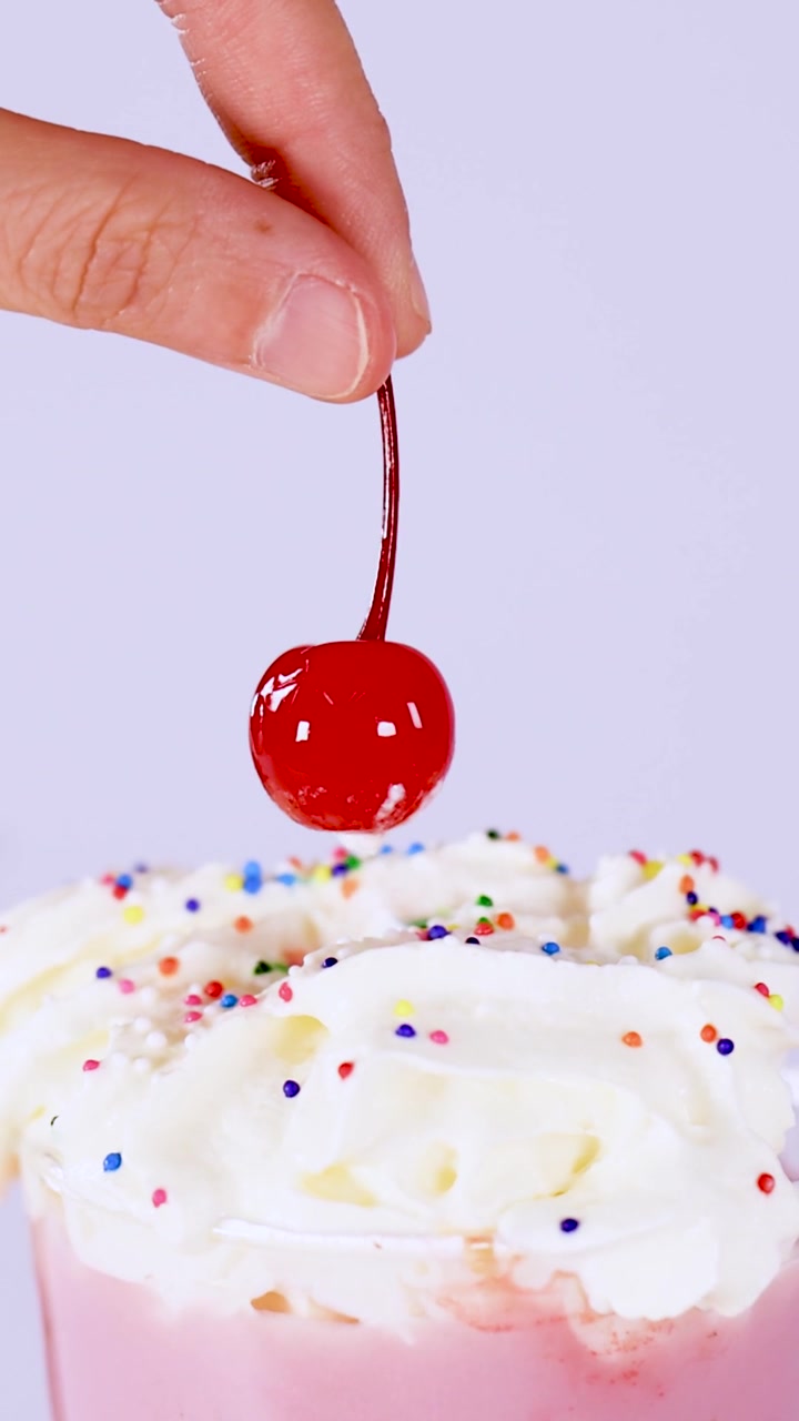 Primo piano di dita che sollevano una ciliegia rossa dalla panna montata e dalle codette su un milkshake.