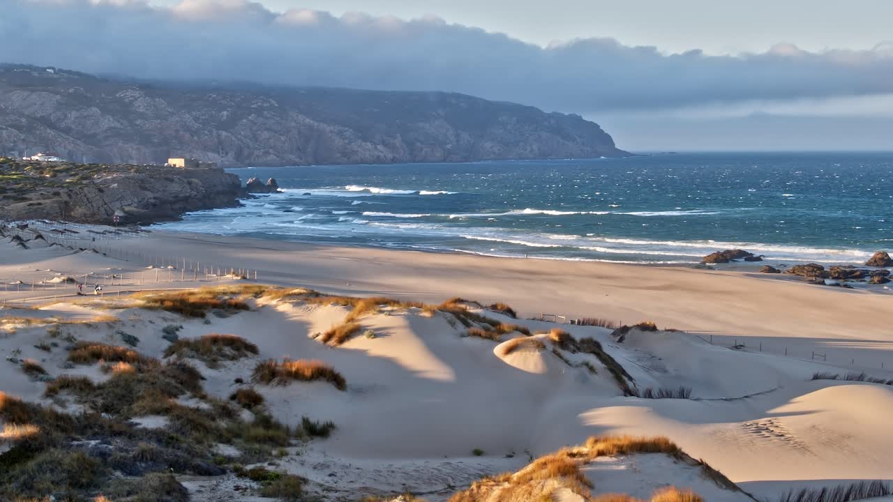 View of sandy beach and waves in Portugal with hills in background