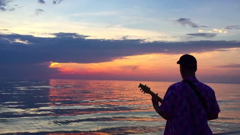 handheld on man with back to camera playing a busker toy guitar to the setting sun on a beautiful evening at georgian bay