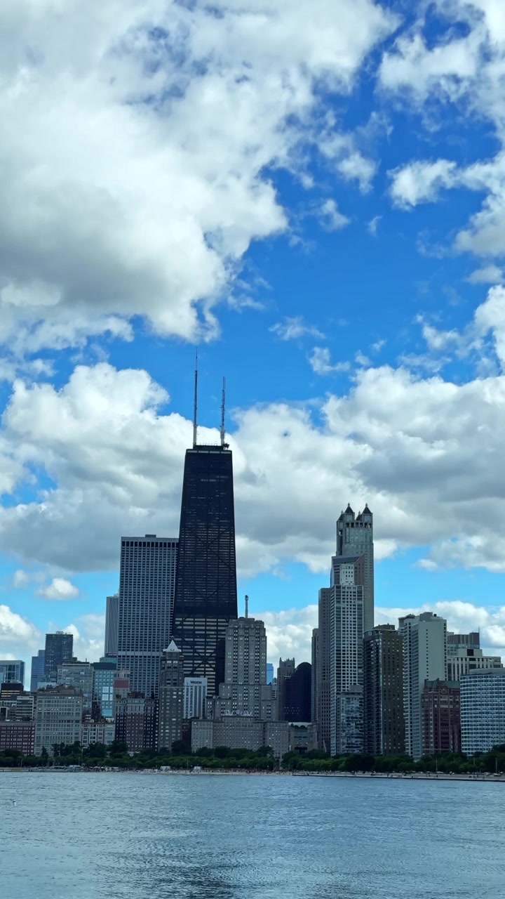 Nuvole fluttuano sopra uno skyline cittadino con grattacieli di giorno, con un cielo azzurro brillante sullo sfondo che mostra la loro architettura moderna.