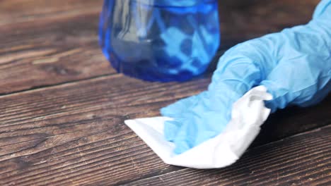 cleaning a wooden table with blue gloves and cleaning supplies