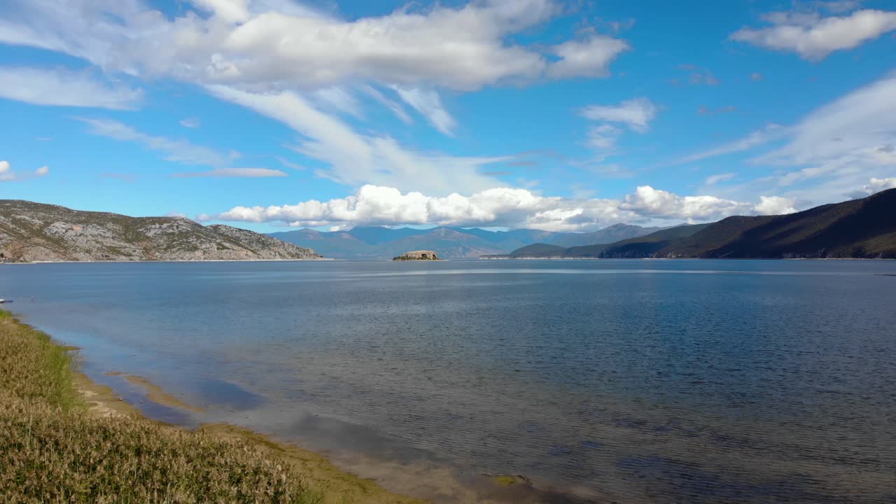 берег горного озера преспа с зелеными камышами осенью, белые облака на голубом небе