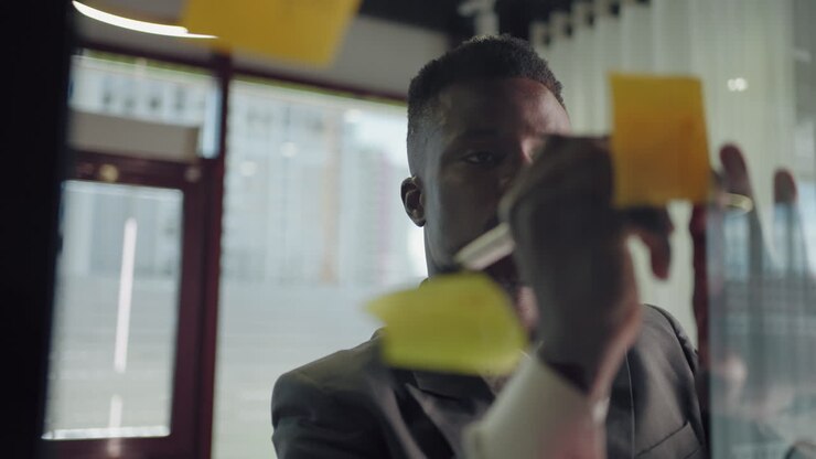 African American businessman working with sticky notes in office. Entrepreneur explaining business plan. Businessman building mind map with sticky notes on glass
