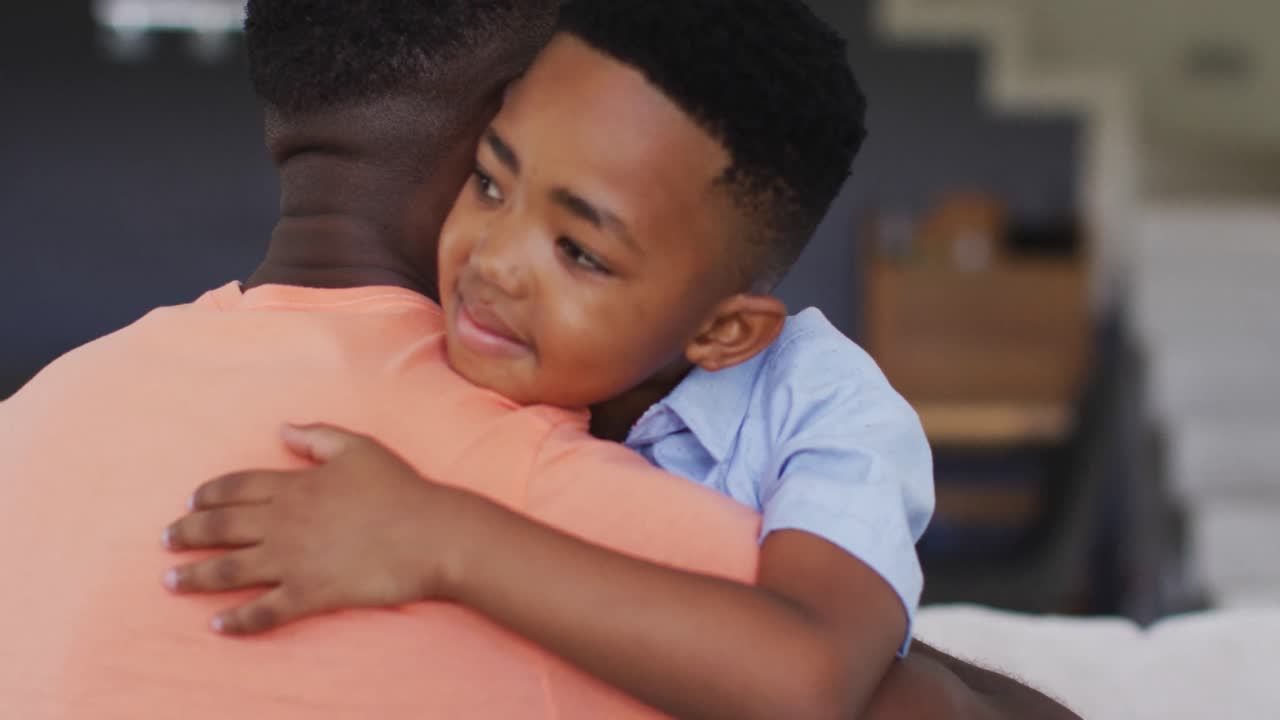 padre y hijo afroamericanos abrazándose en un sofá