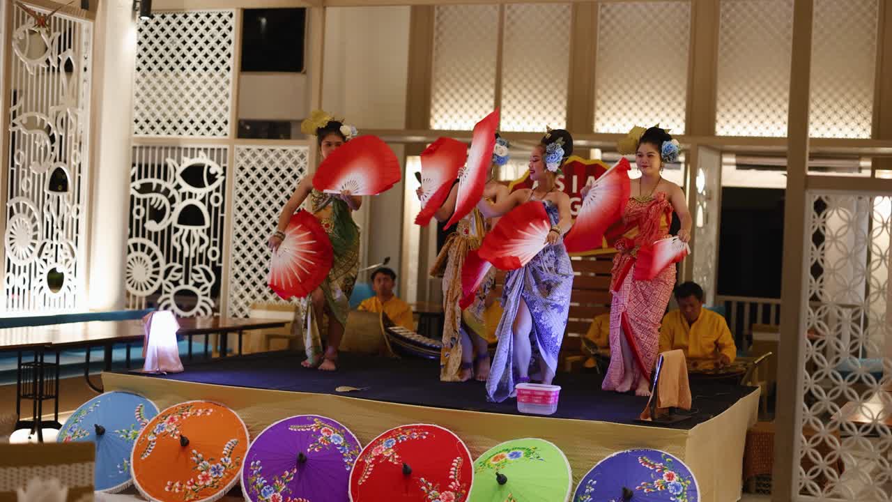 다채로운 의상과 팬을 가진 활기찬 전통 춤, 태국 레스토랑의 장식된 무대에서 여성들에 의해 수행됩니다.