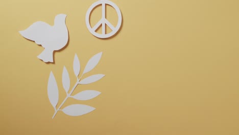 close up of white dove with peace sign and leaf and copy space on yellow background