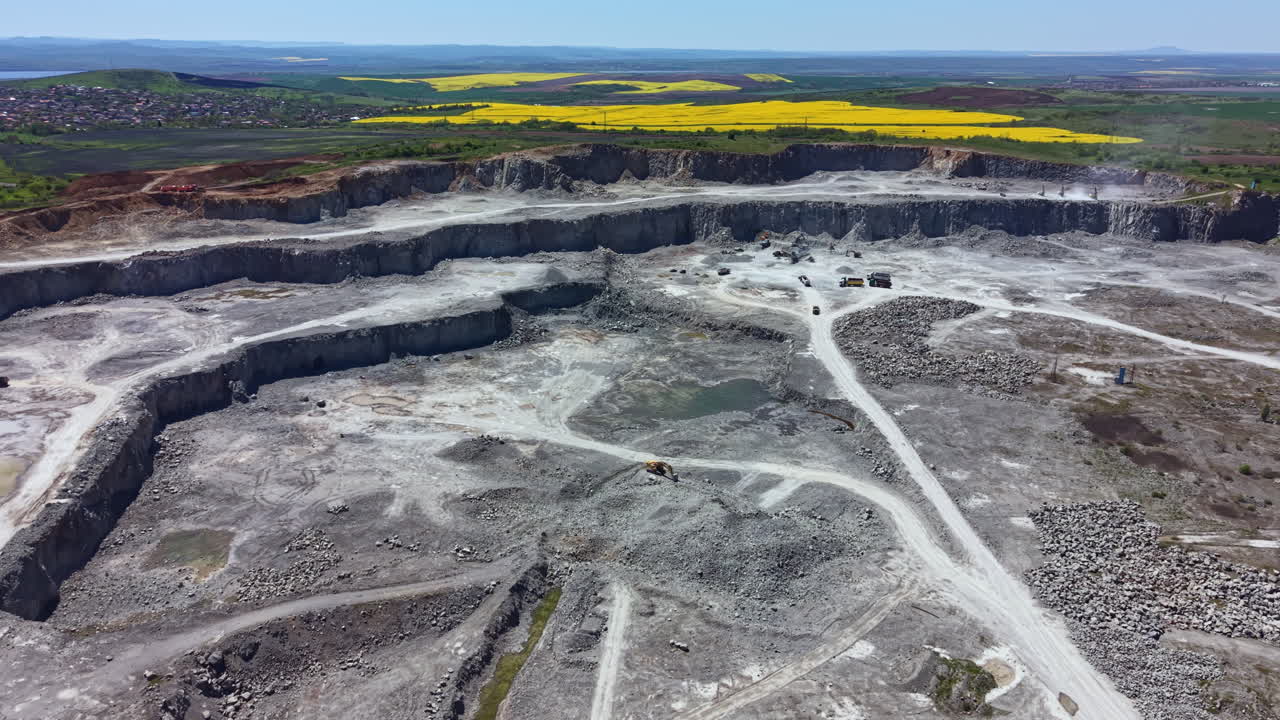 View of a large quarry site with heavy machinery and a bright landscape in the background during daytime operation