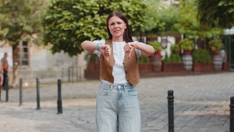 upset young caucasian woman lady showing double thumbs down expressing discontent on city street