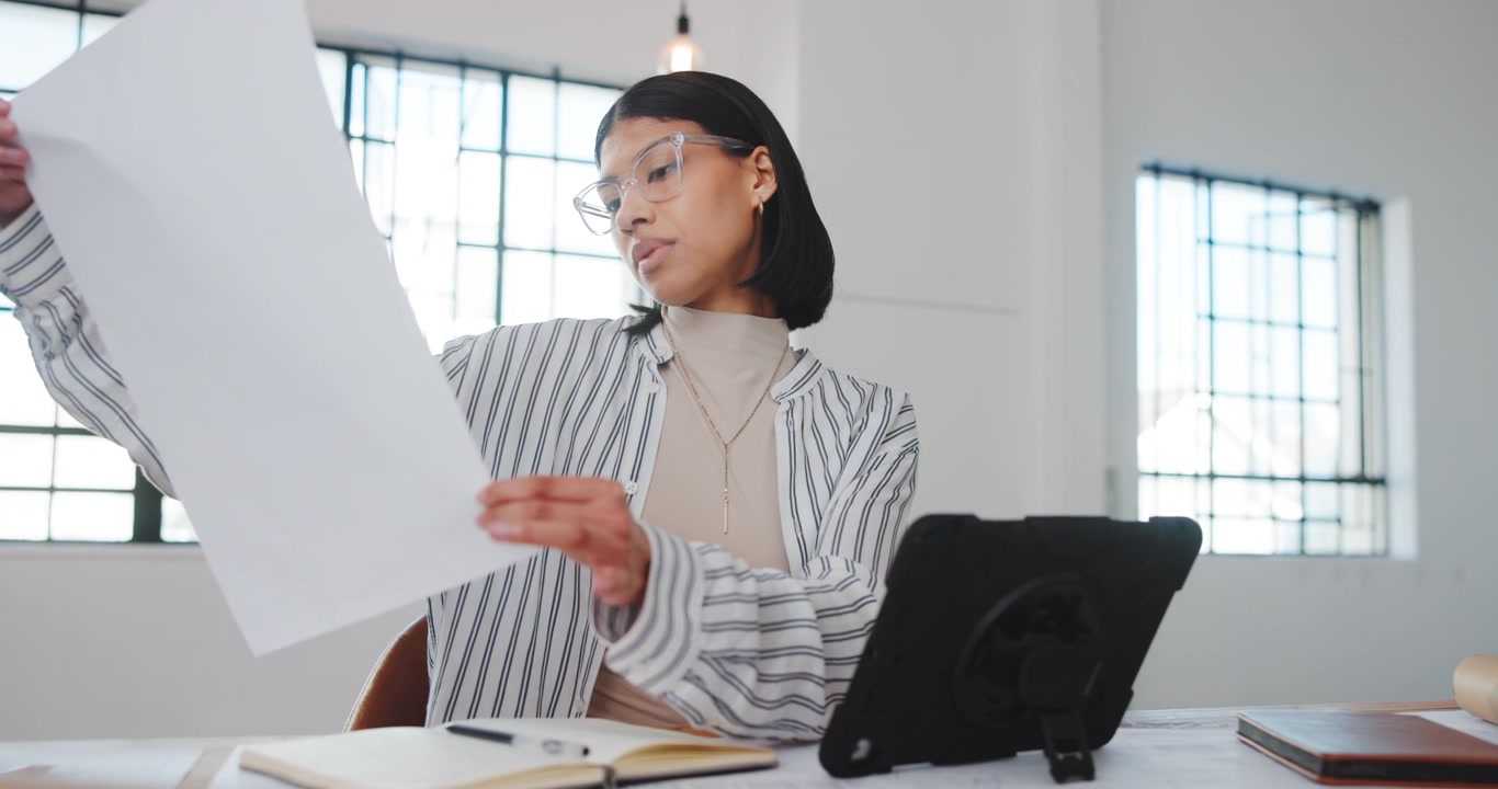 Young Woman Reviewing Architectural Plans and Using Tablet in Office