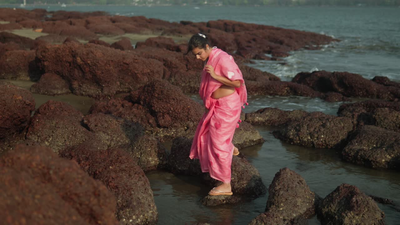 joven con vestido rosa explorando la costa rocosa, las olas chocando cerca, aventura a la luz del día