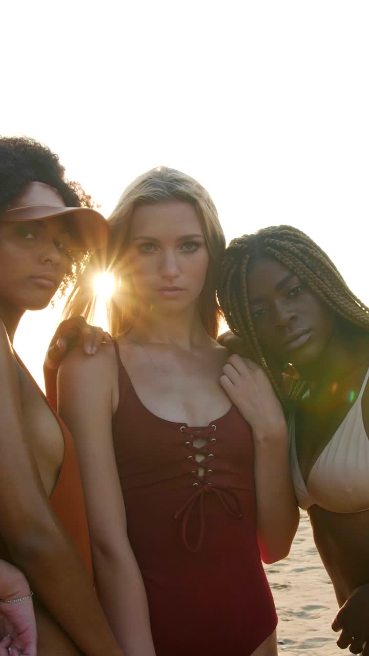 Tre donne in costume da bagno sedute vicine sulla spiaggia con un forte bagliore solare in video verticale.