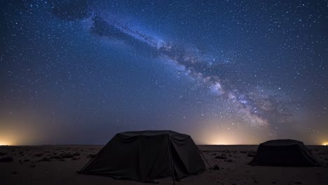 camping tents pitched on sandy desert ground, starry milky way arching overhead, revealing stunning celestial landscape during tranquil nighttime wilderness experience