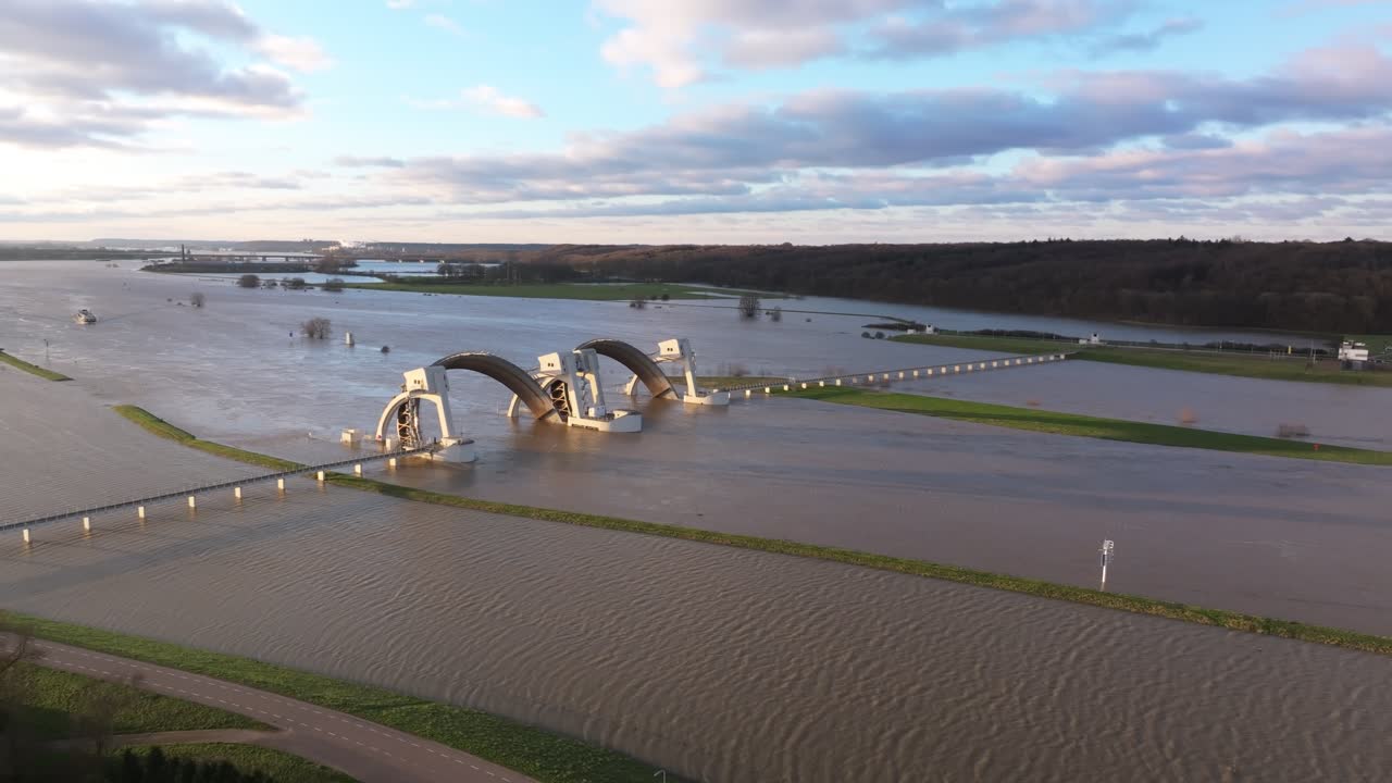 Aerial orbit drone shot at the weir of Driel during high water levels with the doors open and with a cargo ship arriving in the background