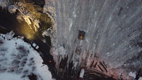 bulldozers work at snow depot after storm, overhead aerial push-in