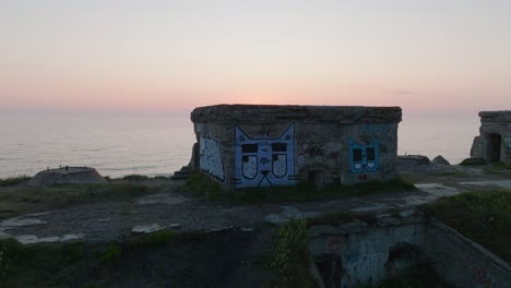 Beautiful-aerial-view-of-vibrant-high-contrast-sunset-over-calm-Baltic-sea,-clouds-at-the-horizon,-Karosta-war-port-concrete-coast-fortification-ruins-at-Liepaja,-wide-drone-dolly-shot-moving-left