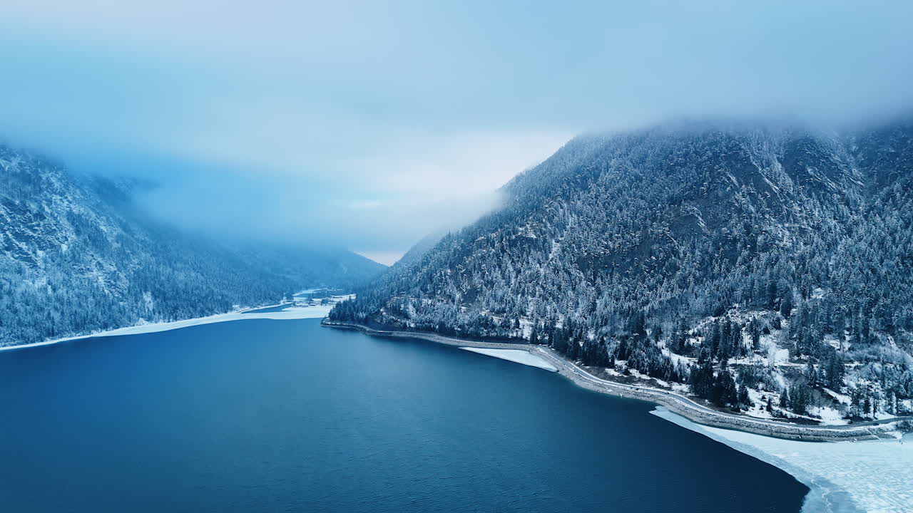 Beautiful winter in the mountainous area. Drone footage over the grey waterscape of a big lake. Germany, Europe.
