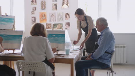 slow motion old people attend drawing courses. the teacher helps pensioners who attend drawing courses to draw. a group of retired friends at a drawing lesson