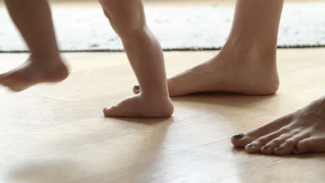 barefoot infant learning walking with help of mother on floor