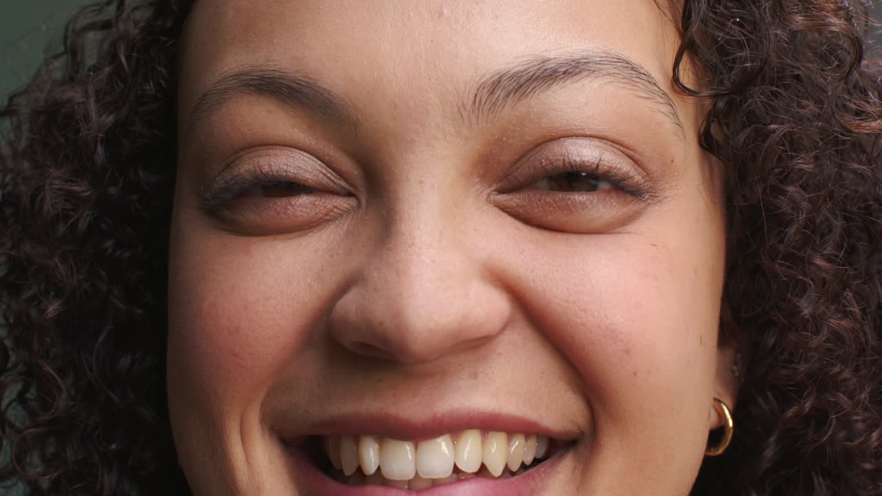 African American woman reacting to camera smiling eyes opening curly hair gold hoop muted wall