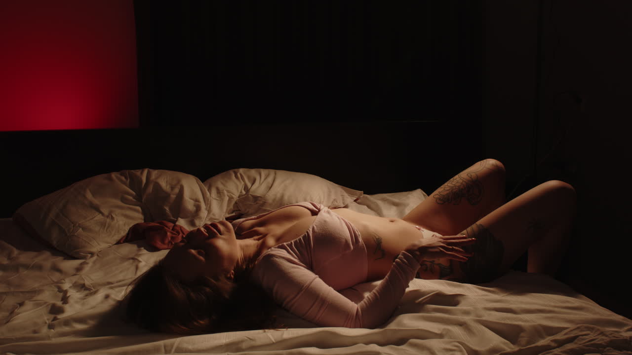 Stunning wide view of a sensual woman wearing seductive lingerie lying down on a bed in a dark bedroom