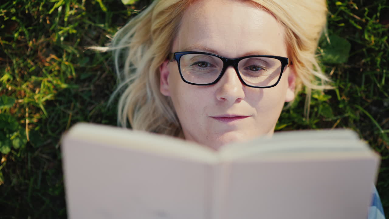 Portrait Of A Young Woman In Glasses Lying On A Lawn In The Park And Reading A Book 4k Video