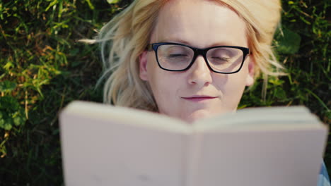 portrait of a young woman in glasses lying on a lawn in the park and reading a book 4k video