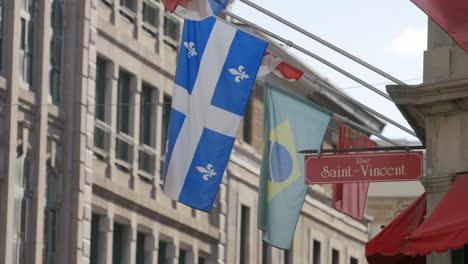 Bandera-De-Quebec-Y-Bandera-Brasileña-En-El-Exterior-De-Un-Edificio-Comercial-En-La-Esquina-De-Rue-Saint-vincent-En-El-Viejo-Montreal,-Quebec,-Canadá