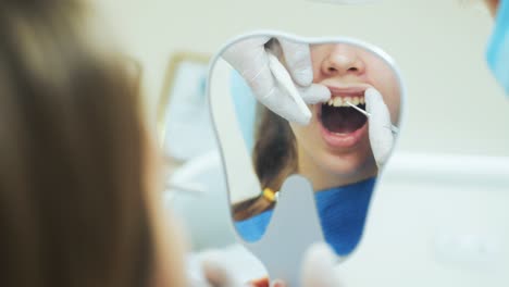 a girl at the dentist looks in the mirror as a doctor treats teeth with medical instruments. close-up
