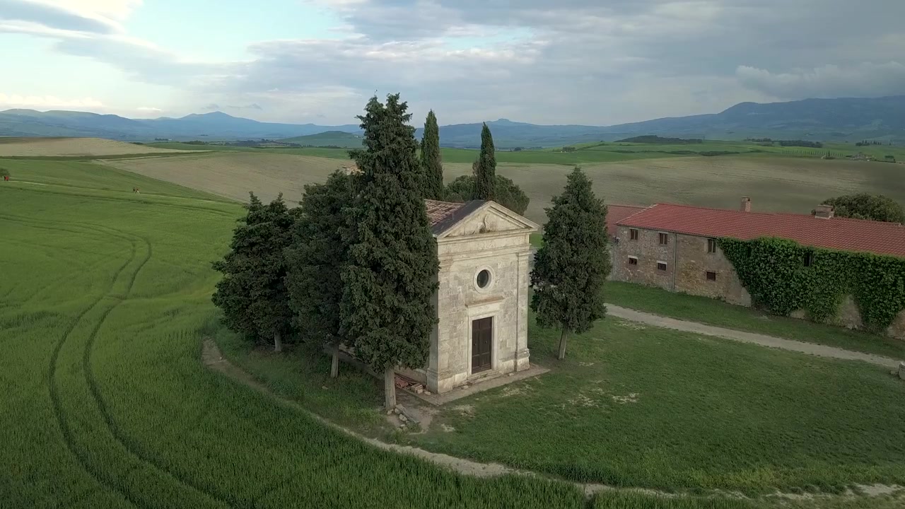 [Riprese aeree] Innalzandosi sopra un campo di grano e volando verso la Cappella di Vitaleta in Toscana, Italia.