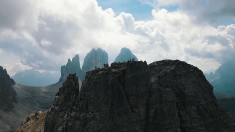 five mountaineers atop the di lavaredo at the cross while the partly cloudy tre cime emerges in the background