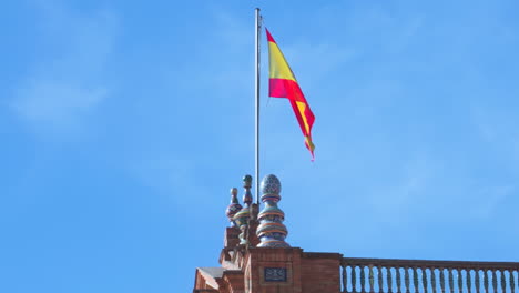 spanish flag waving on top of one of the towers of plaza de españa in seville