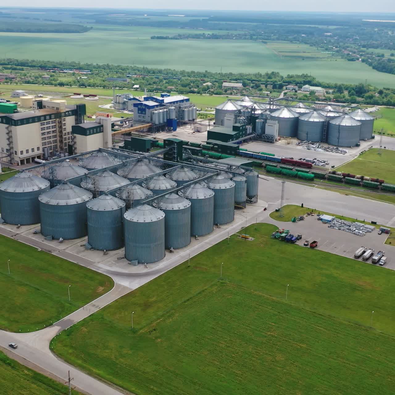 Agricultural factory among nature. Elevator for grain storage. Grain storage tanks on green field. Aerial view.